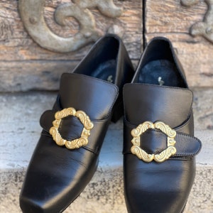 May include: A pair of black leather shoes with gold buckles. The buckles have a decorative design.