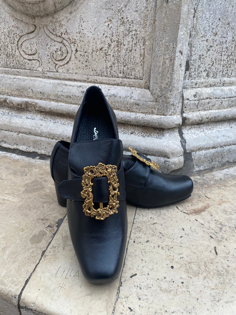 May include: A pair of black leather shoes with gold ornate buckles. The shoes have a pointed toe and a low heel.