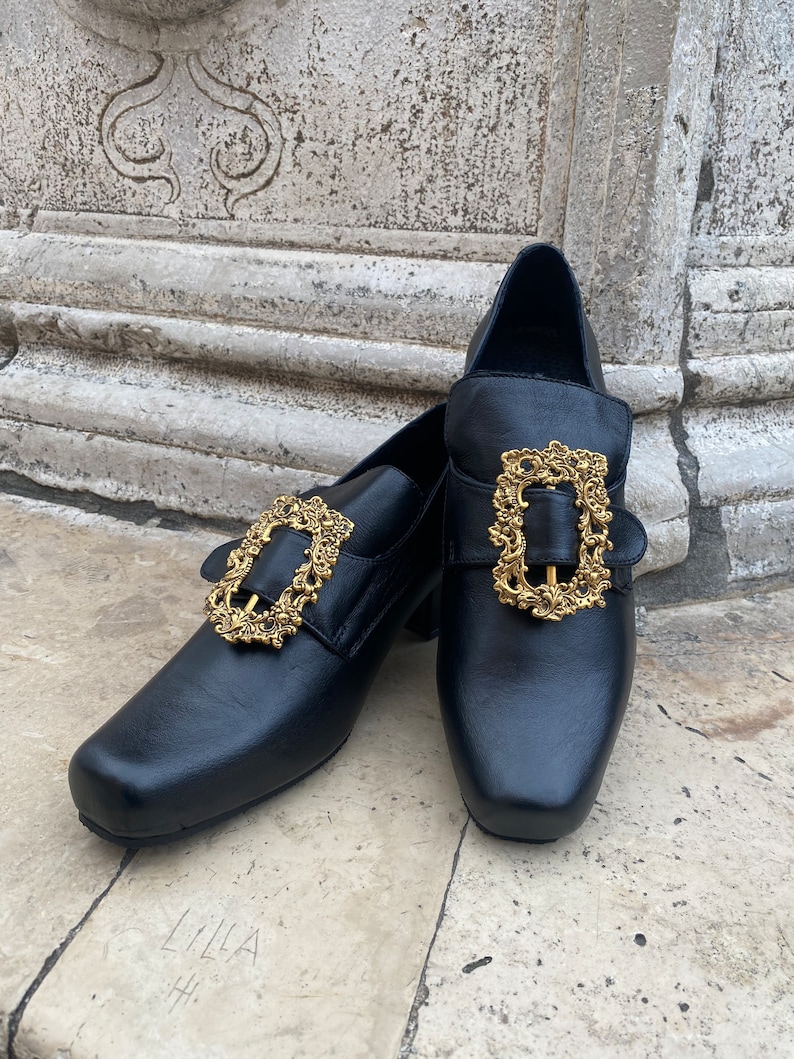 May include: A pair of black leather shoes with gold ornate buckles. The shoes have a square toe and a low heel.