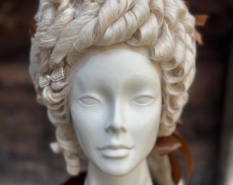 May include: A white wig with large, curled ringlets. The wig is styled in a high, elaborate fashion with brown ribbons and a gold hair clip.