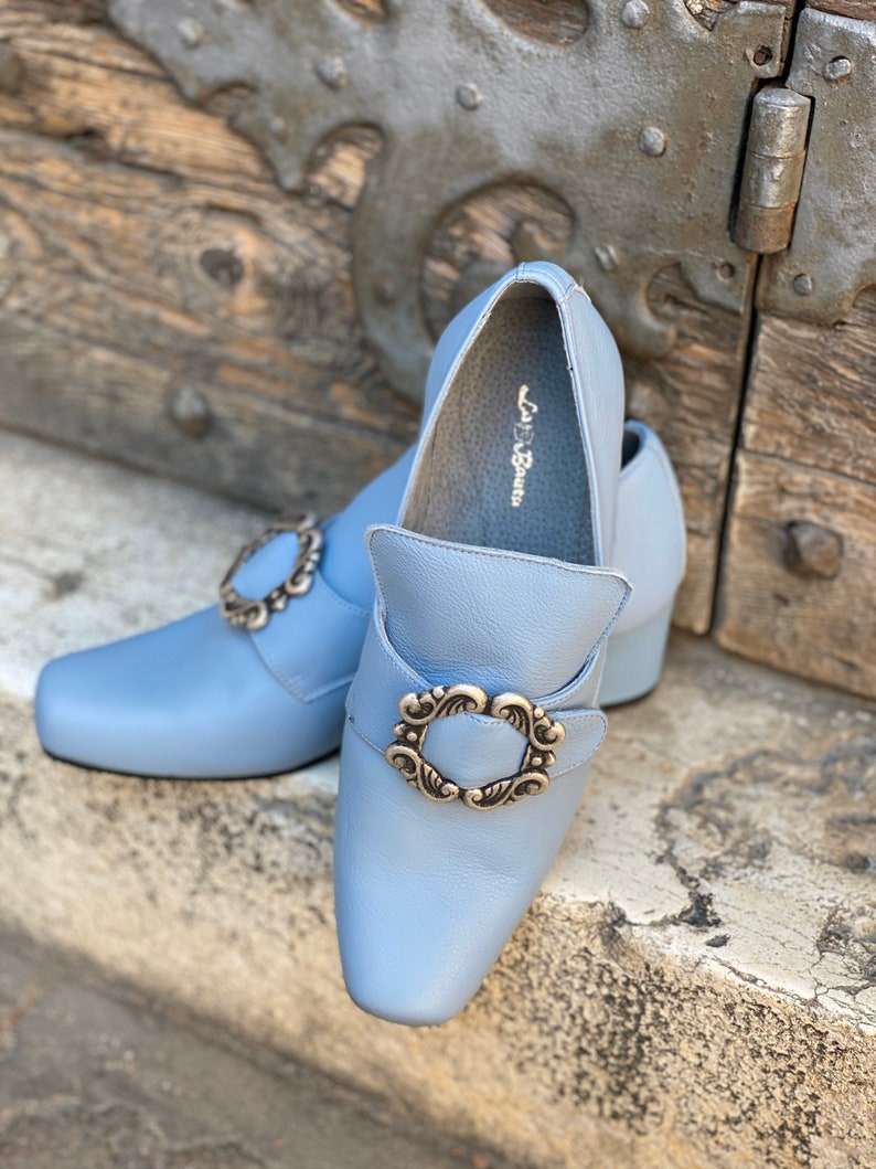 Puede incluir: Un par de zapatos de cuero azul claro con una hebilla plateada decorativa. Los zapatos tienen una punta puntiaguda y un tac&oacute;n bajo. El nombre de la marca "La Botte" es visible en el interior de un zapato.