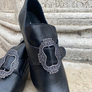 May include: A pair of black leather shoes with silver buckles. The buckles have an ornate design.