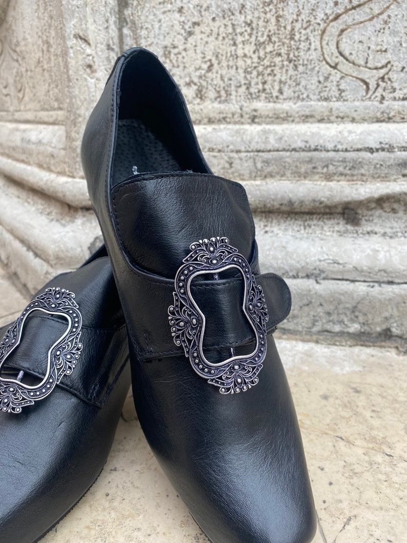 May include: A pair of black leather shoes with silver buckles. The buckles have an ornate design.