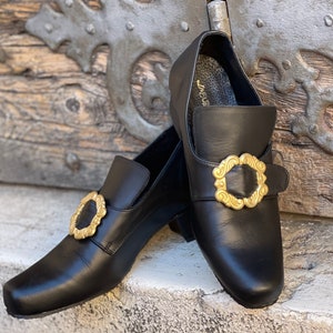 May include: A pair of black leather shoes with gold buckles. The shoes have a pointed toe and a low heel.