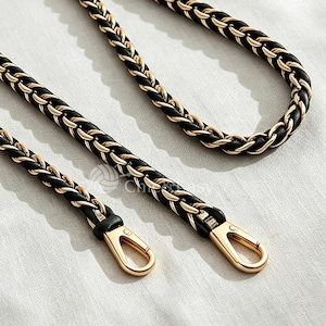 May include: A long, braided bag strap featuring a combination of black material and polished gold-tone metal links. The strap is looped into an oval shape and includes two gold-tone metal lobster claw clasps at the ends for secure attachment.