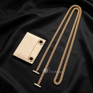 May include: A gold-toned metal chain strap with two T-bar ends and a rectangular beige felt attachment featuring two gold-toned metal grommets. The chain is long and folded, and the small logo text Chic&Easy is visible near the chain.