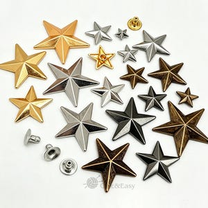 Könnte beinhalten: Eine Sammlung von sternförmigen Metallnieten und Nieten in verschiedenen Größen und Ausführungen, darunter poliertes Gold, Silber, Rotguss und antike Bronze. Das Set enthält mehrere einzelne Sternkomponenten und passende runde Metallrückseiten.