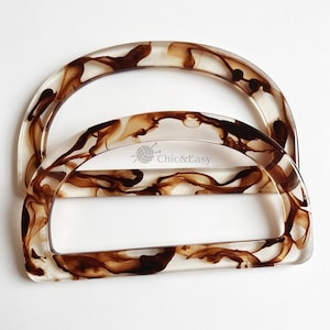 May include: Two semi-circular bag handles made of clear resin with a swirling brown marbled pattern. The front handle features the text Chic&Easy with a small yarn ball icon printed in the centre. The handles have a smooth, glossy finish.