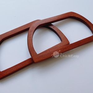 May include: Two wooden handles for a bag, both are brown and have a rounded shape. The handles are stacked on top of each other.
