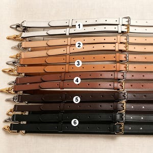 Könnte beinhalten: Sechs verstellbare Taschenriemen, horizontal angeordnet und von 1 bis 6 nummeriert. Die Riemen verfügen über Metallschnallen und Karabinerhaken und sind in einem Farbverlauf von Weiß über Beige, Hellbraun, Braun, Dunkelbraun bis Schwarz.
