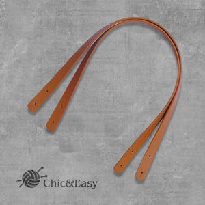 Puede incluir: Dos correas de cuero marrón con costuras, aptas para usar como asa de bolso.