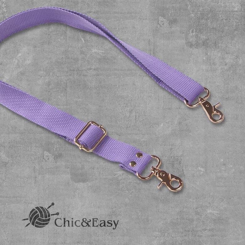 May include: A lavender adjustable strap with gold metal hardware, including a buckle and two swivel clasps. Chic&Easy is printed on the strap.