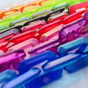 Może przedstawiać: Zbliżenie na kolekcję kolorowych, zazębiających się plastikowych ogniw łańcucha. Ogniwa ułożone są w rzędach, prezentując gradient kolorów od pomarańczowego do niebieskiego. Ogniwa są przezroczyste i prawdopodobnie używane do rękodzieła lub tworzenia biżuterii.