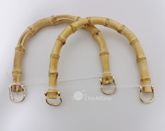 Puede incluir: Dos asas de bolso de bambú natural con herrajes de metal dorado. Las asas son curvadas y tienen un aspecto natural y rústico.