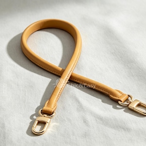 Puede incluir: Una correa de bolso color amarillo mostaza con un diseño redondeado y acolchado con costuras a tono. La correa cuenta con cierres de mosquetón de metal dorado en ambos extremos. El texto Chic&Easy está impreso en blanco en el centro.