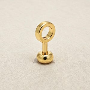 May include: A gold-toned metal stud earring featuring a circular ring top attached to a straight post and a smooth, rounded base. The piece has a polished, reflective surface and includes the small text Chic&Easy printed near the base.