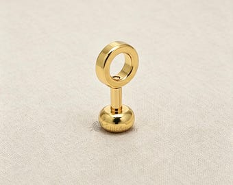 May include: A gold-toned metal stud earring featuring a circular ring top attached to a straight post and a smooth, rounded base. The piece has a polished, reflective surface and includes the small text Chic&Easy printed near the base.