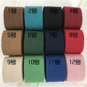 Puede incluir: Doce rollos de cinta de algod&oacute;n tejido en varios colores, incluyendo marr&oacute;n, azul verdoso, negro, rojo, beige, verde, azul marino, rosa y crema. Cada rollo est&aacute; etiquetado con un n&uacute;mero del 1 al 12.