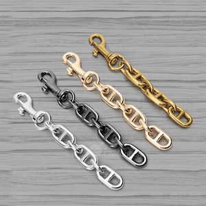 May include: Four metal chain leash attachments in silver, black, gold, and brass. Each chain has a lobster claw clasp on one end and a series of oval links on the other. The chains are displayed on a gray wooden surface.