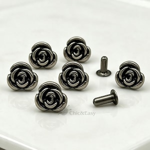 May include: A collection of gunmetal-colored metal rivets shaped like three-dimensional roses. The set includes several rose-shaped caps and two matching cylindrical metal posts. The text Chic&Easy is visible in the lower center area.