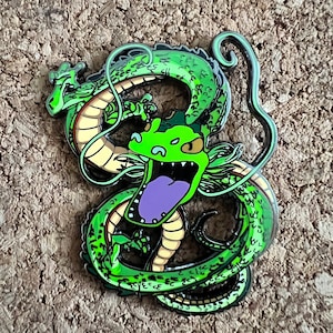 Puede incluir: Pin de esmalte de dragón verde con contornos negros y lengua morada. El dragón está enroscado con su cola en la boca.