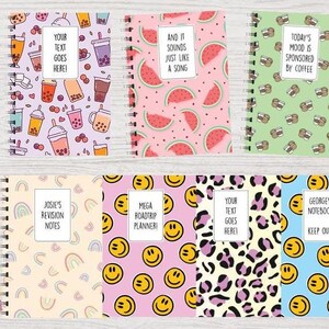 May include: Six different designs of spiral notebooks. The designs include bubble tea, watermelon, coffee cups, rainbows, smiley faces, and leopard print. The notebooks have text on the front, such as "Your text goes here!" and "Today's mood is sponsored by coffee."