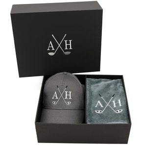 May include: A black gift box with a gray baseball cap and a gray towel inside. The cap and towel both have the letters "AXH" embroidered on them with crossed golf clubs.
