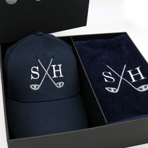 May include: A navy blue golf hat and towel set with the initials "SH" embroidered in white with crossed golf clubs. The set is packaged in a black gift box.
