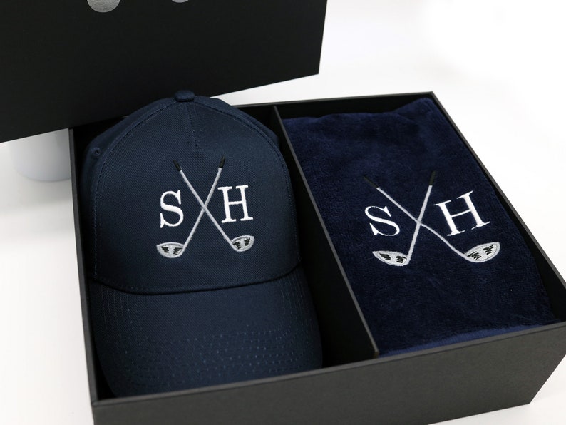 May include: A navy blue golf hat and towel set with the initials "SH" embroidered in white with crossed golf clubs. The set is packaged in a black gift box.