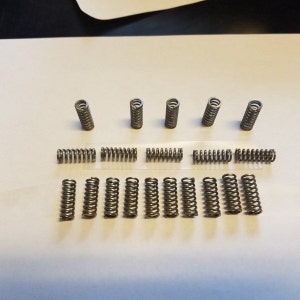 May include: A collection of 20 silver metal springs of varying sizes. The springs are arranged in two rows on a white surface.