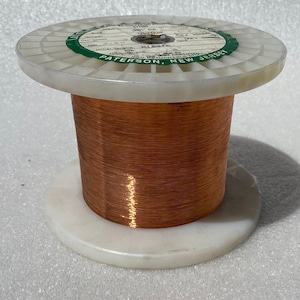 May include: A spool of copper wire with a white plastic base and a green label that reads "EL. CONDUCTOR 01706 TEMPERED 0061" DIA. 204,000 PSI.  TENSILE  NON-CERTIFIED  PATERSON, NEW JERSEY",