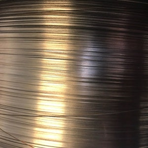 May include: Close-up of a spool of shiny silver wire. The wire is tightly wound and reflects light.
