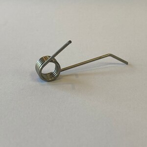 May include: A silver spring with a coiled section and a bent arm.