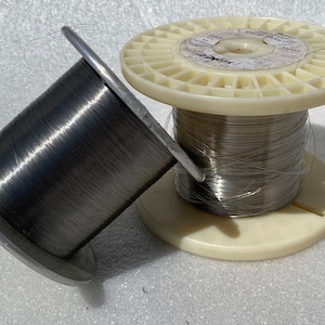 May include: Two spools of silver wire, one on a white plastic spool with a label that reads "INCONEL 600", and the other on a plain spool.
