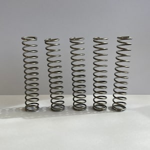 May include: Five silver metal springs, all the same size, are lined up in a row on a white surface.