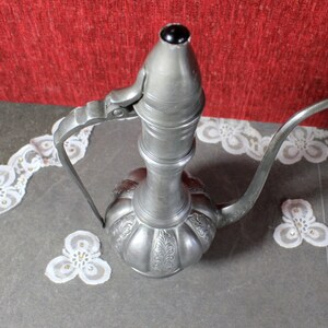 May include: A silver metal teapot with a long spout and a handle. The teapot has an ornate design and a round body.
