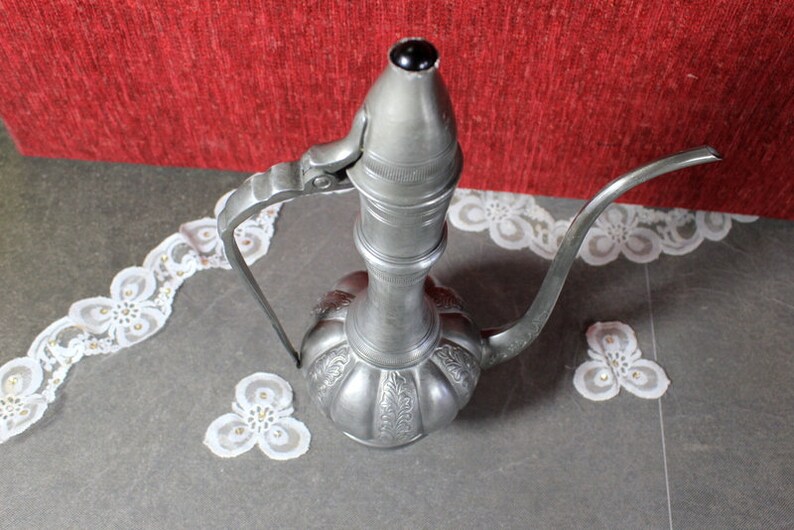 May include: A silver metal teapot with a long spout and a handle. The teapot has an ornate design and a round body.
