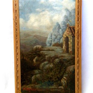 May include: A framed oil painting depicting a stone building with a doorway, set against a backdrop of rocky hills and a cloudy sky. The painting is signed "M. Cadonna" in the lower right corner.