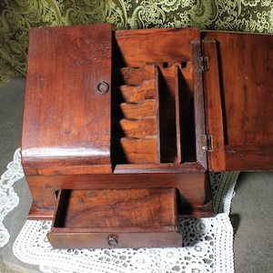 Op de afbeelding: Een vintage houten bureau-organizer met een rijke, donkerbruine afwerking. De organizer heeft meerdere compartimenten, een kleine lade en scharnierende deuren. Het open ontwerp onthult interne opslagruimtes.