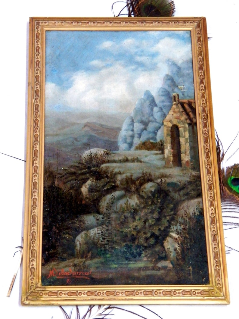 May include: A framed oil painting depicting a landscape with a small stone building in the foreground. The building has a rounded archway and a stone roof. The background features a rocky hillside with a blue sky and white clouds. The painting is signed "M. Macdonald" in the lower right corner.