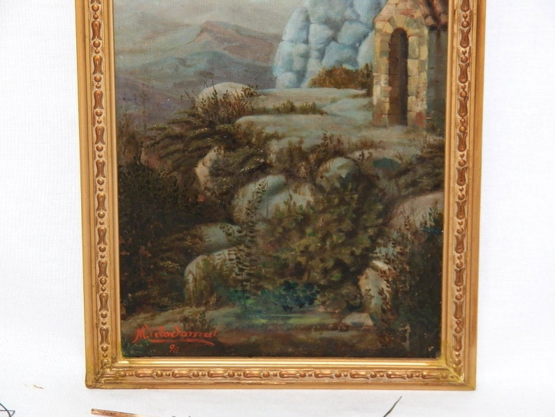 May include: A framed oil painting depicting a landscape scene with a stone building and a mountain in the background. The painting is signed "M. Macdonald" in the lower right corner.