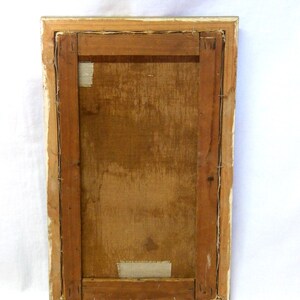May include: The back of a framed painting with a wooden frame and a canvas stretched over a wooden stretcher bar. The canvas is secured with staples and there is a piece of tape on the back of the canvas.
