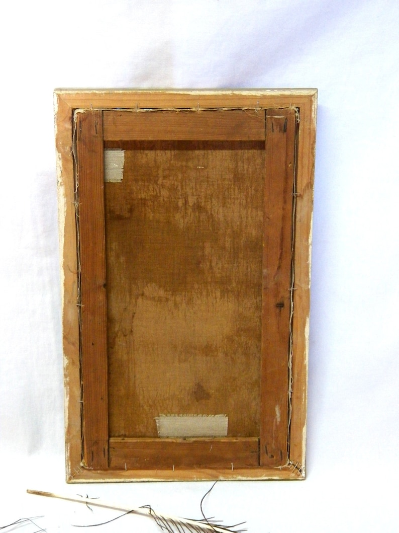 May include: The back of a framed painting with a wooden frame and a canvas stretched over a wooden stretcher bar. The canvas is secured with staples and there is a piece of tape on the back of the canvas.