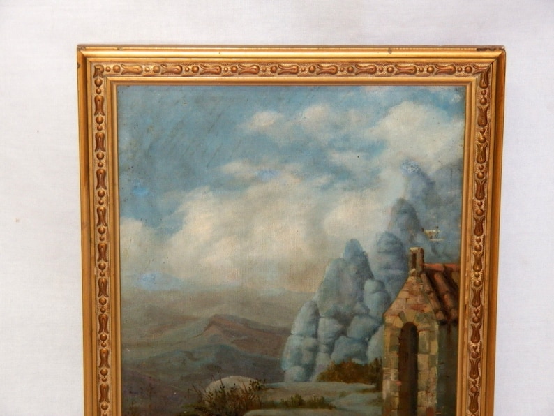 May include: A framed oil painting depicting a landscape with a stone building in the foreground. The building has a rounded archway and a stone roof. The background features a mountainous landscape with a cloudy sky.