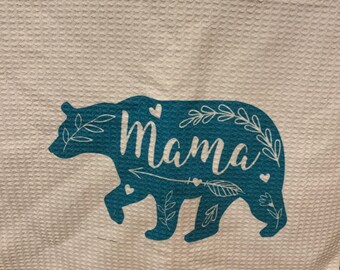 Puede incluir: Toalla de cocina blanca con una silueta de oso azul. El oso tiene la palabra "Mama" escrita en su interior. El oso está rodeado de pequeños diseños florales y corazones.