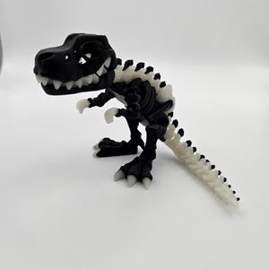 May include: A black plastic dinosaur skeleton toy with white bones. The dinosaur is standing on a white surface.