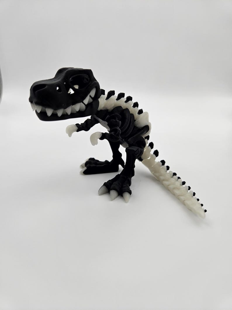 May include: A black plastic dinosaur skeleton toy with white bones. The dinosaur is standing on a white surface.