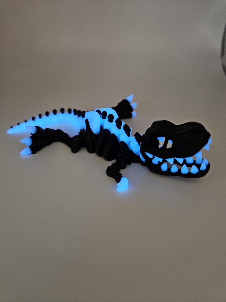 May include: A black glow-in-the-dark dinosaur skeleton figurine. The dinosaur is posed in a running position with its mouth open and teeth visible. The skeleton is made of plastic and has a smooth, glossy finish.