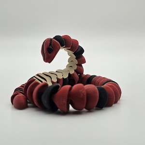 May include: A red and black segmented snake toy made of plastic. The snake is curled up in a coil.