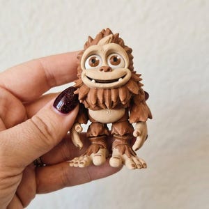 Op de afbeelding: Een klein, bruin, 3D-geprint figuurtje van een wezen met grote, ronde ogen, een brede glimlachende mond en gestructureerde vachtachtige details. Het personage heeft een lichtbruine buik, puntige oren en zichtbare lijnen van het printproces.